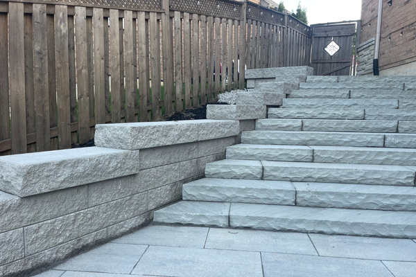 Armour stone retaining wall with interlocking steps on a tiered sloped backyard in the GTA