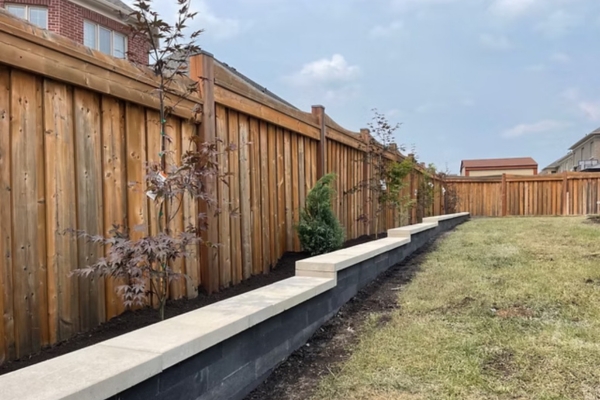 Interlocking block retaining wall holding a grade change along a residential backyard fence line in the GTA
